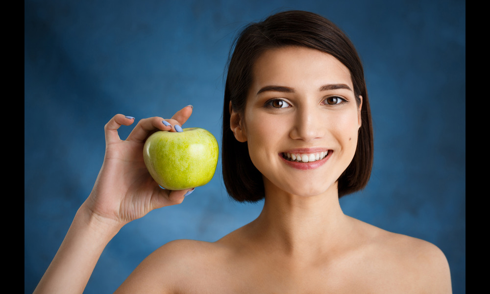 A girl smiling with white teeth holding an apple, teeth whitening near me.