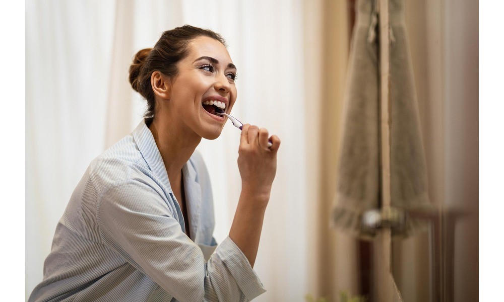 A woman brushing her teeth after cosmetic dentistry treatment