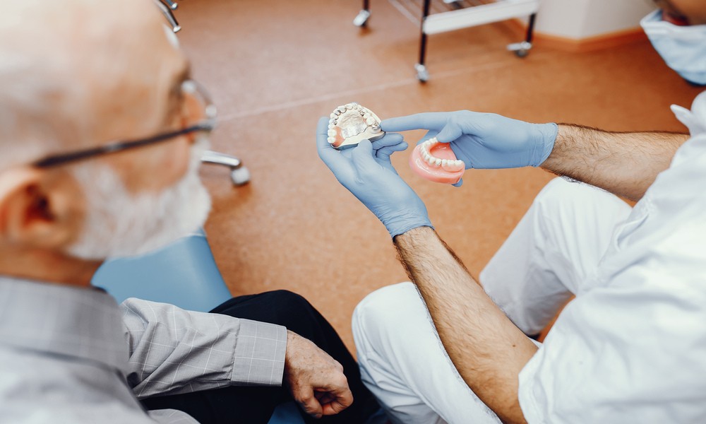 Dentist holding loose dentures of senior patient